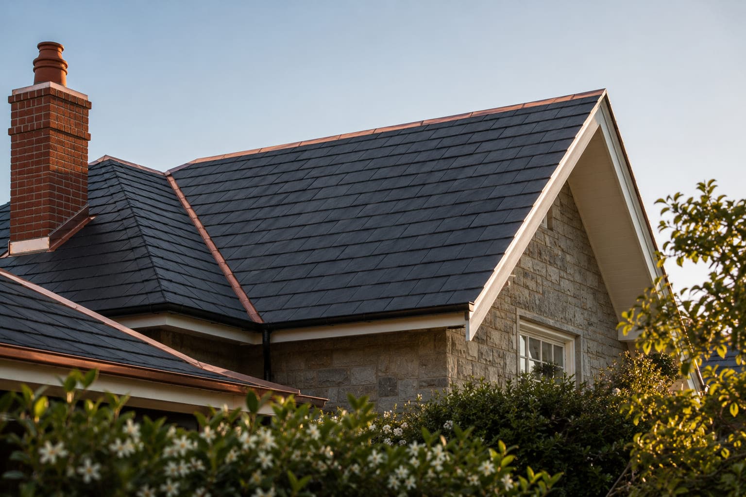 Completed natural slate roof with copper flashings on a stone home